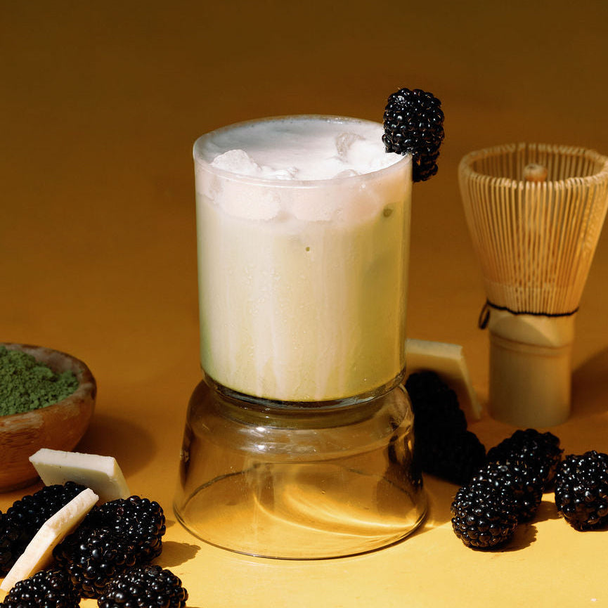 Glass of matcha with blackberries and matcha powder on a yellow background