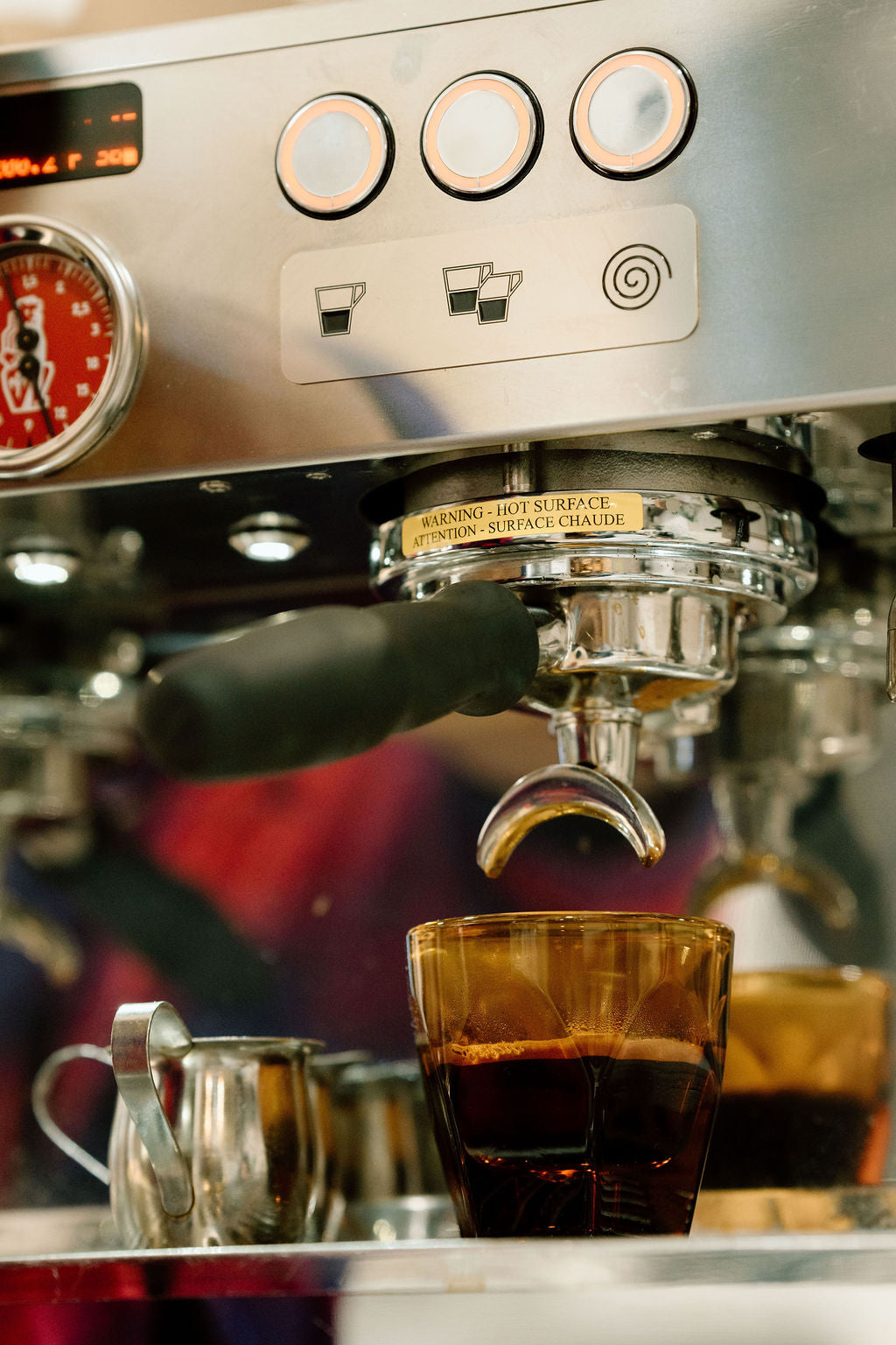 Espresso machine dispensing coffee into a glass cup with various coffee-making equipment around.