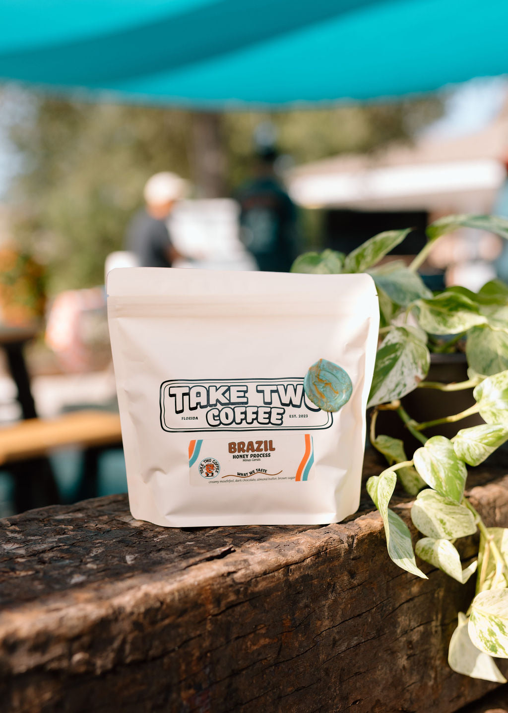 Coffee bag labeled 'Take Two Coffee' on a wooden surface with a blurred outdoor background