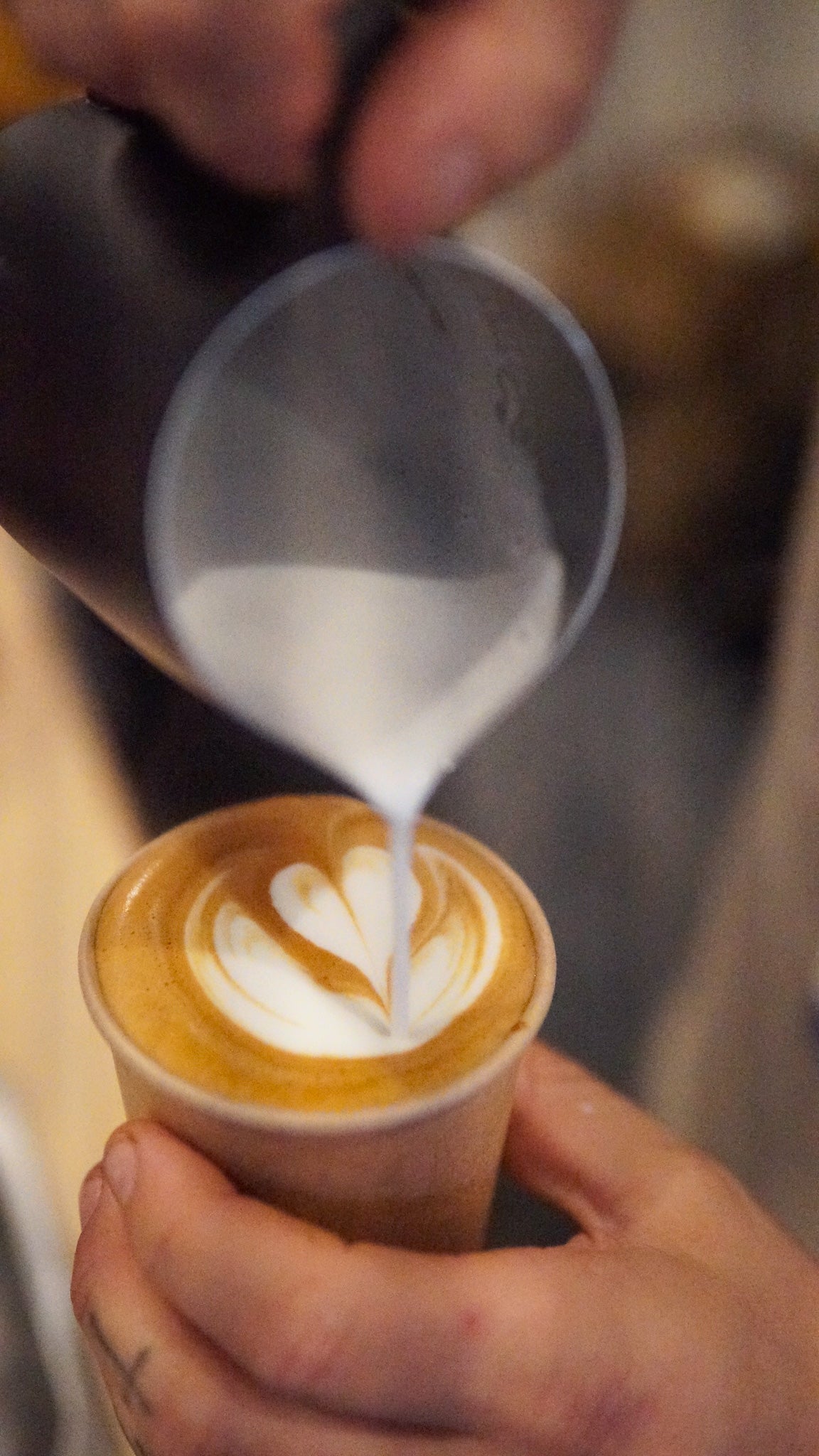 Person pouring milk into a cup of coffee to create latte art.