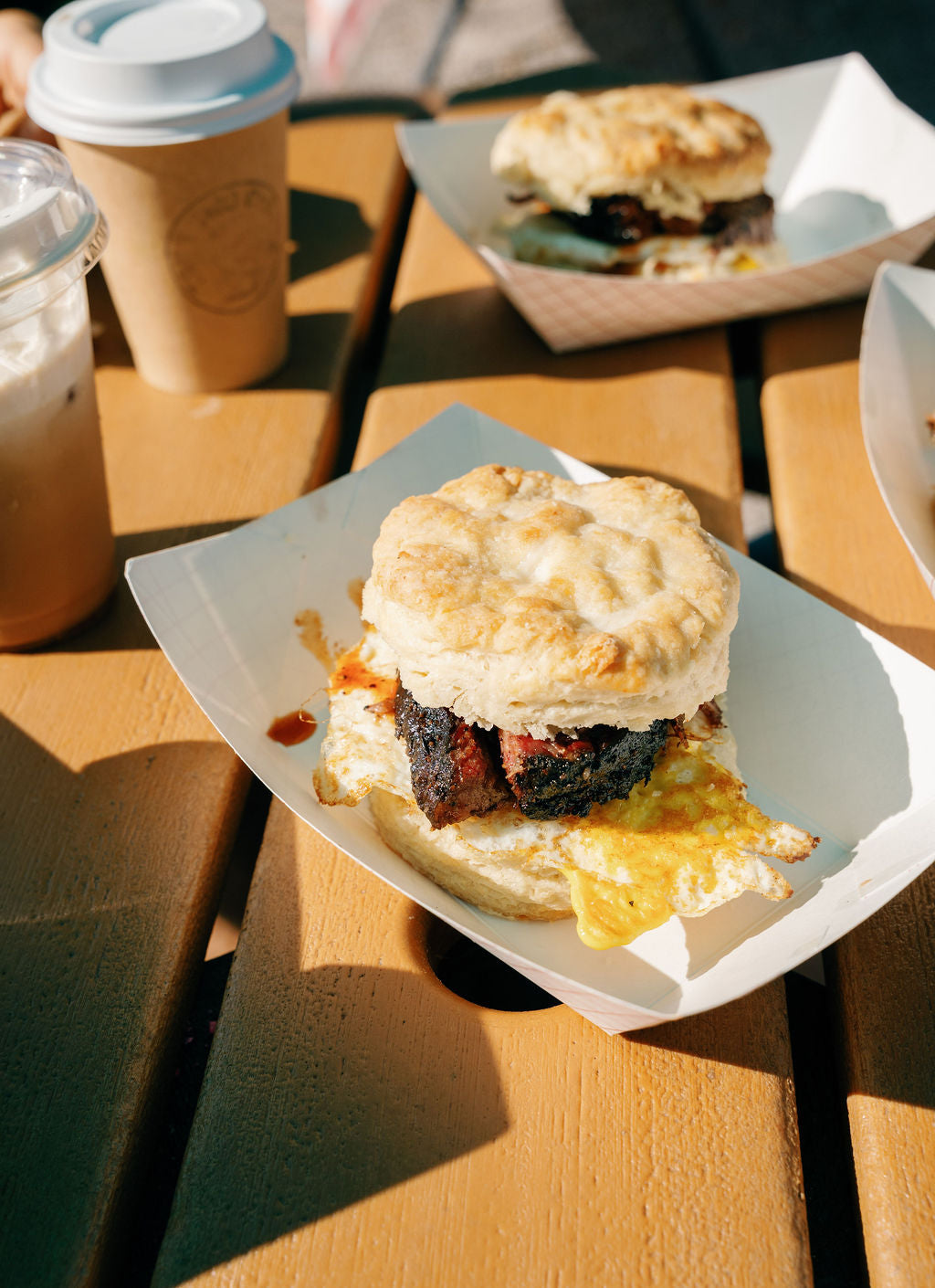 Biscuit sandwich on a paper plate with a coffee cup in the background